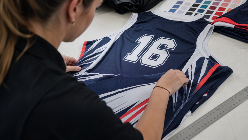 Garment technician checking sublimated jersey fabric, seam alignment and number placement.